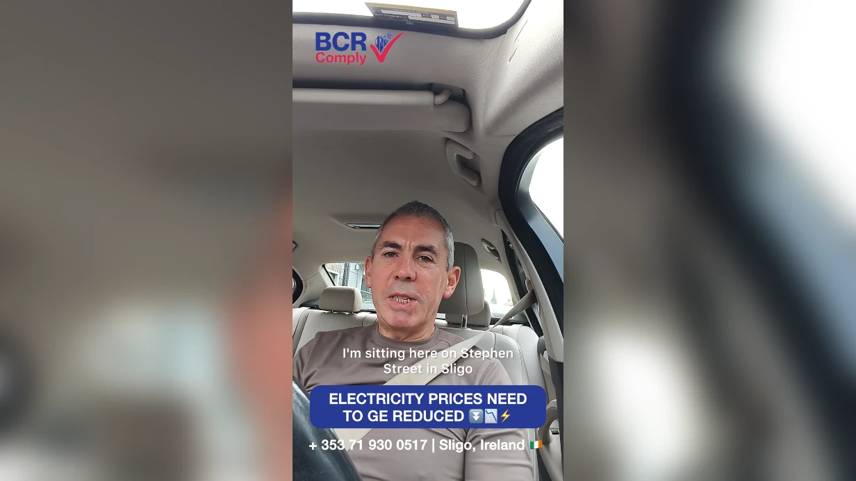 BCR Comply spokesperson discussing electricity prices in a parked car, with the caption Electricity prices need to be reduced