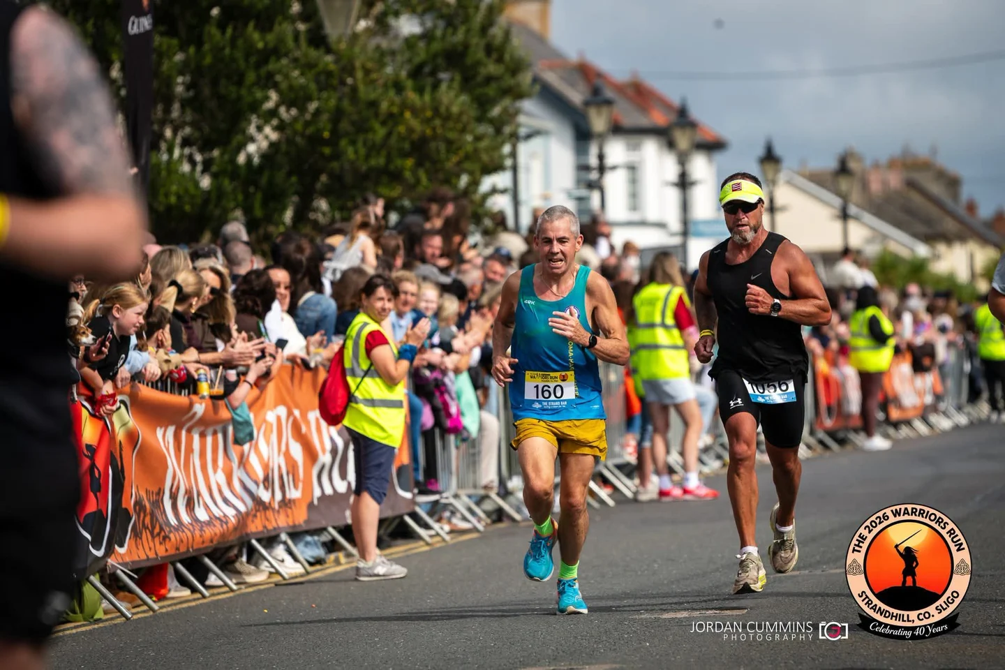 Sean Clancy, race number 160, running beside another competitor as spectators cheer in Strandhill
